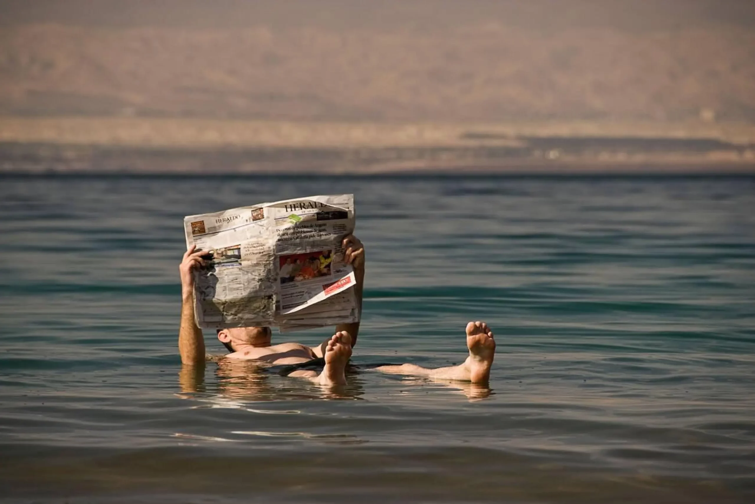 Man reading a newspaper while floating on the Dead sea, Jordan, Asia.
