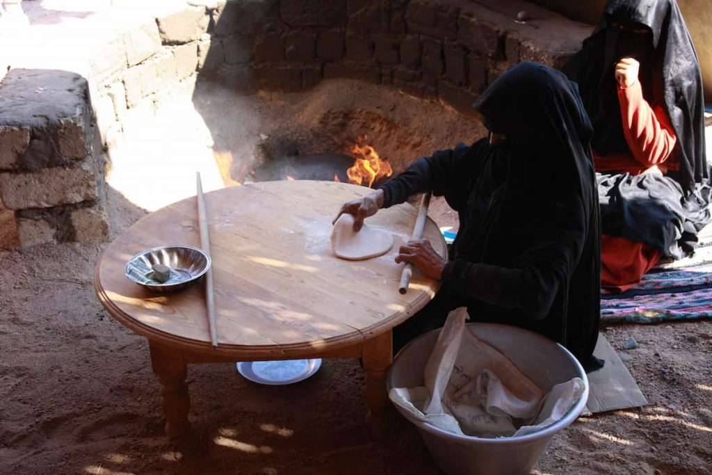  Bedouine woman in traditional costume cooking a bread on the fire