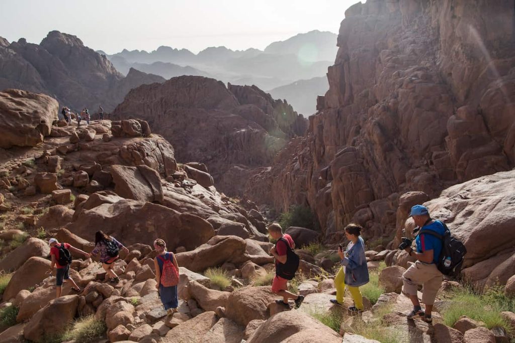 South Sinai, Egypt - May 27, 2019: Travelers walk down the rugged trail on Mount Sinai surrounded by red rock formations and soft morning light in the Sinai Peninsula, Egypt. High quality photo