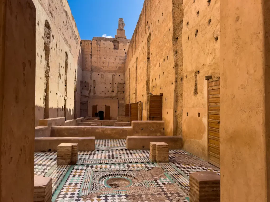 Interior view of El Badi Palace ruins in Marrakech with intricate tile flooring and sunlit walls under a clear blue sky.