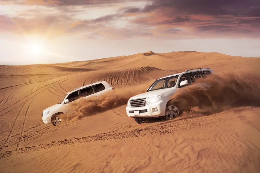 two 4x4 vehicles bashing side to side through the desert dunes in the evening sun 
