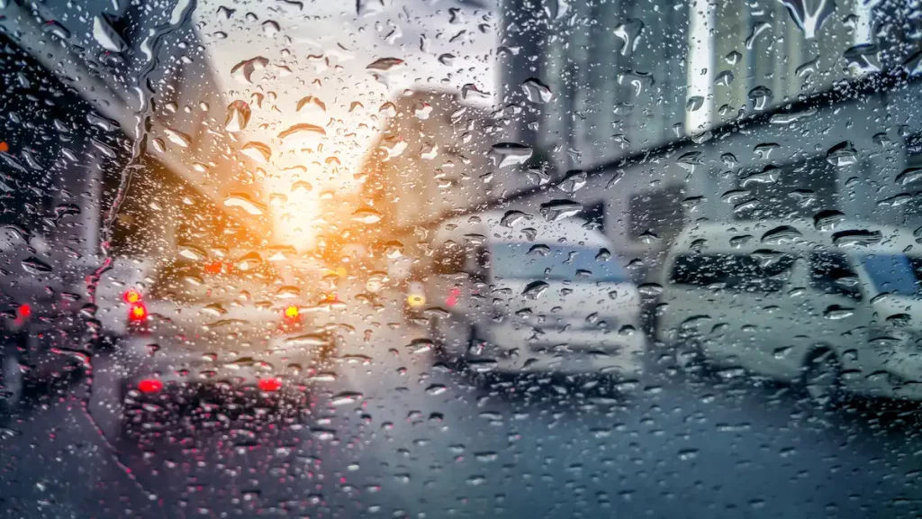 very rare rainy day in bangkok with car lights visible in distance as seen through car windows with rain drops visible on the window.