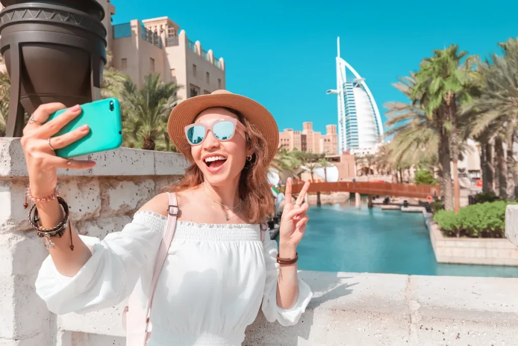 A happy girl takes a photo on her smartphone against the backdrop of the cityscape in Dubai with the hotel Burj al Arab