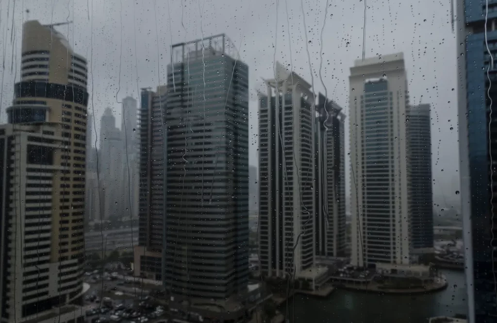 Rainy season in the megacity Dubai. Close up of wet window from which modern commercial skyline of Dubai is visible.