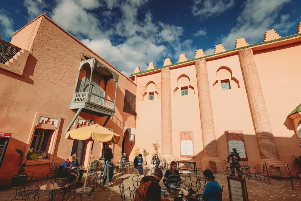 Tourists enjoying a sunny day, seated at tables, sipping drinks and chatting in courtyard of Ben Youssef Madrasa
