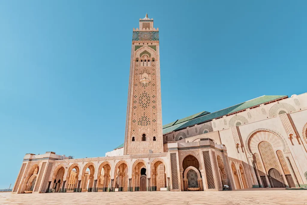 Hassan II Mosque with its minaret towering over the paved square under the vibrant blue sky in Casablanca, Morocco