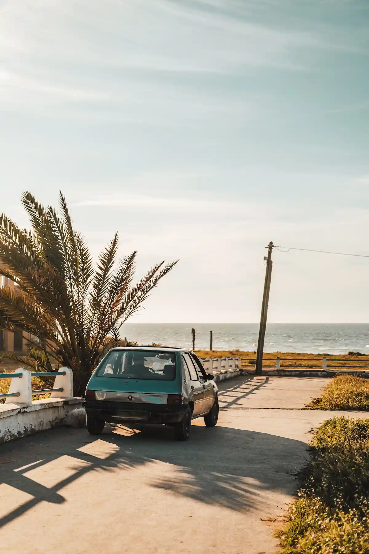  A beautiful shot of a small old car in the sunny park by the beach during sunset in Casablanca, Morocco