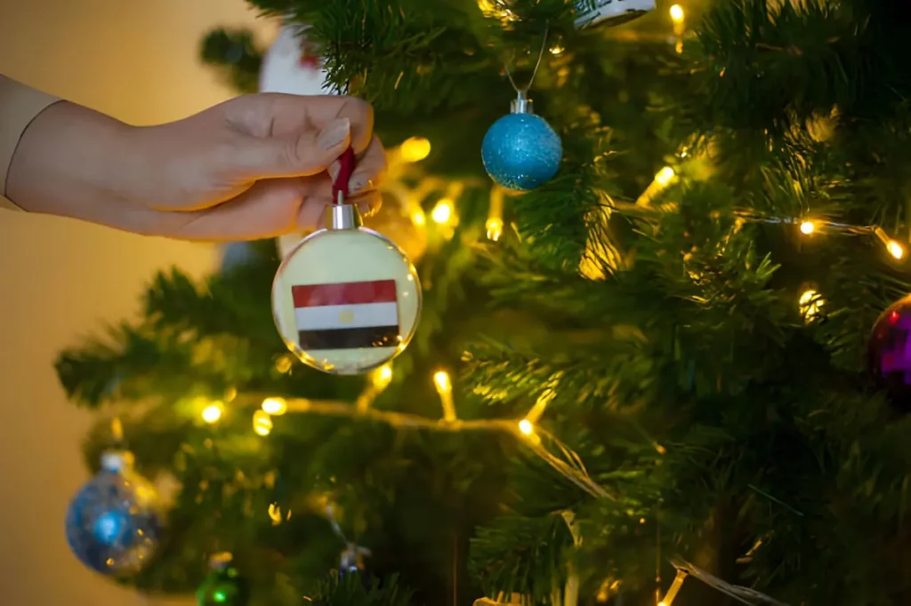 Close up of girls hand holding a Christmas ball for a fir tree with the flag of Egypt. New year in Egypt. New year holiday greeting card with copy space for text. Decorating home for celebration.