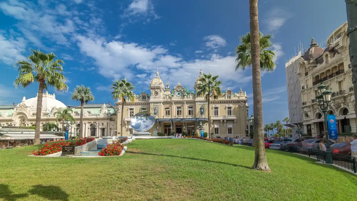 Front view of Grand Casino in Monte Carlo timelapse hyperlapse, Monaco. historical building and square with fountain and green grass. Palms on the side. Blue cloudy sky at summer day