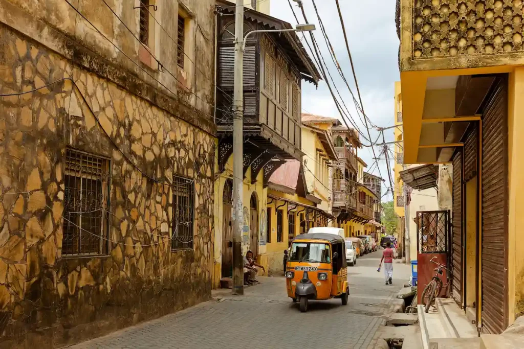 A yellow tuk-tuk rides a narrow street in Mombasa, Kenya.