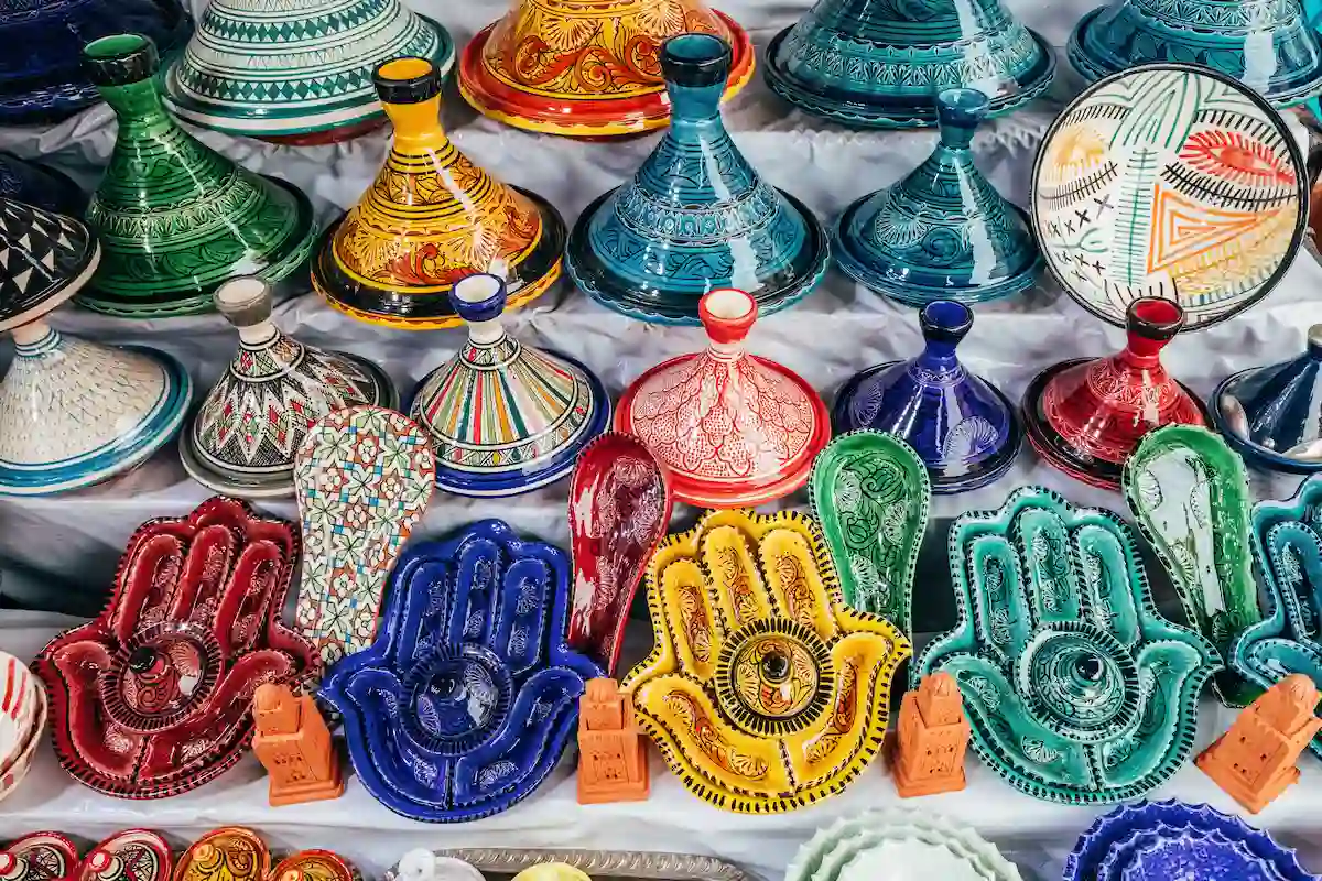 08 March 2025, Marrakech, Morocco: Traditional pottery, including tagines and hamsa shaped dishes, is displayed in vibrant colors at a market stall
