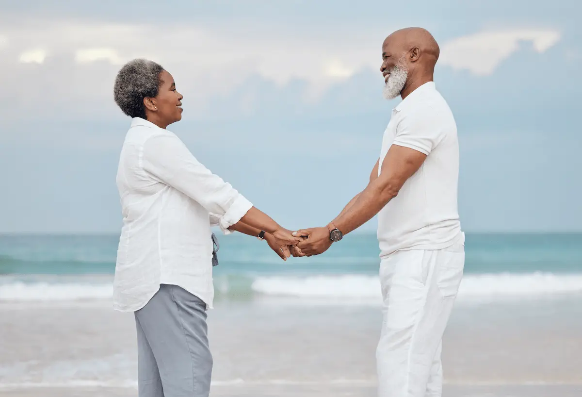 Happy, holding hands and senior couple on beach for travel, vacation or getaway with bonding. Love, connection and elderly man and woman by ocean for retirement holiday together in Morocco.