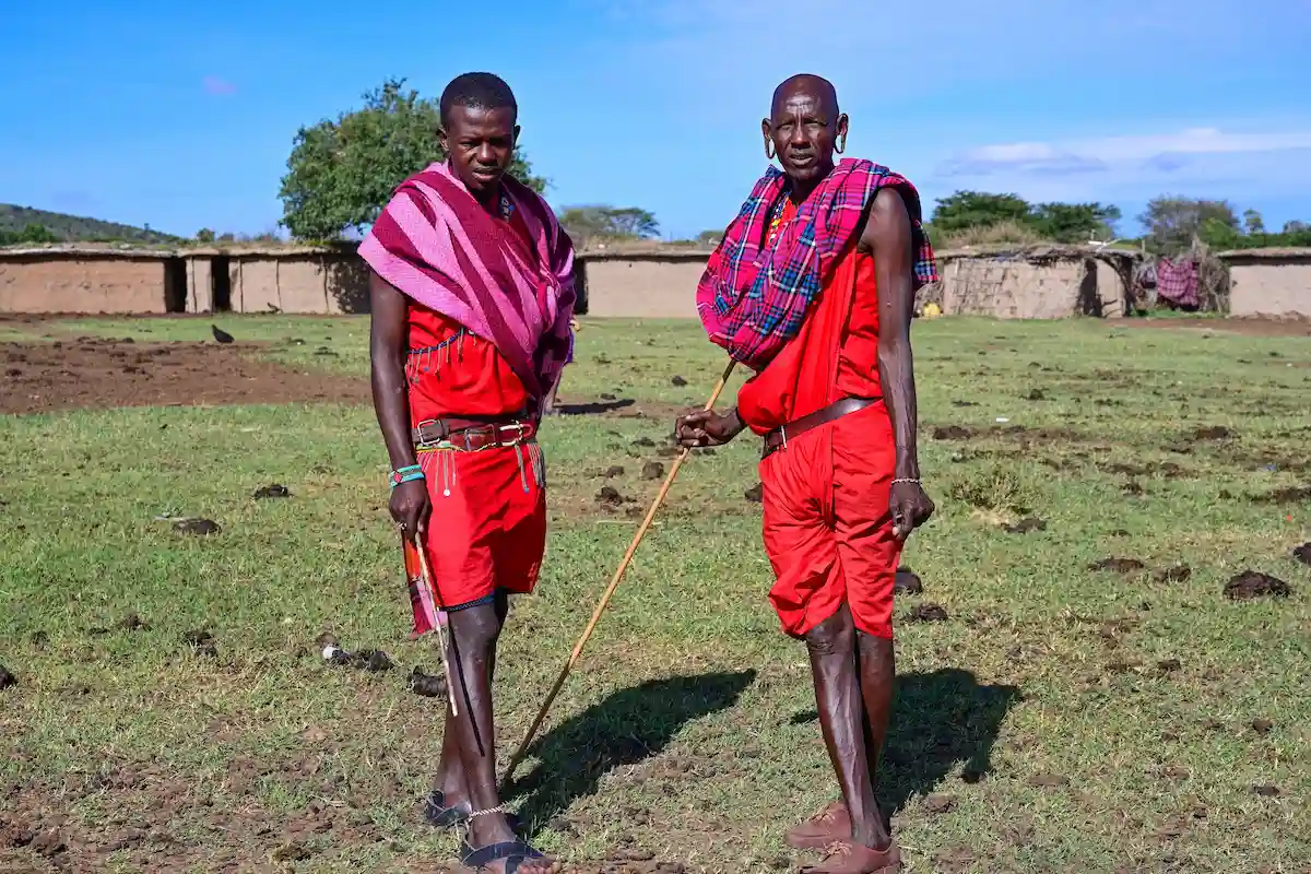 MAASAI MARA NATIONAL RESERVE, KENYA, AFRICA - NOVEMBER 11, 2022: People of Kenya. Two Maasai men in traditional bright clothes stand in the middle of a Maasai village in Kenya, Africa 