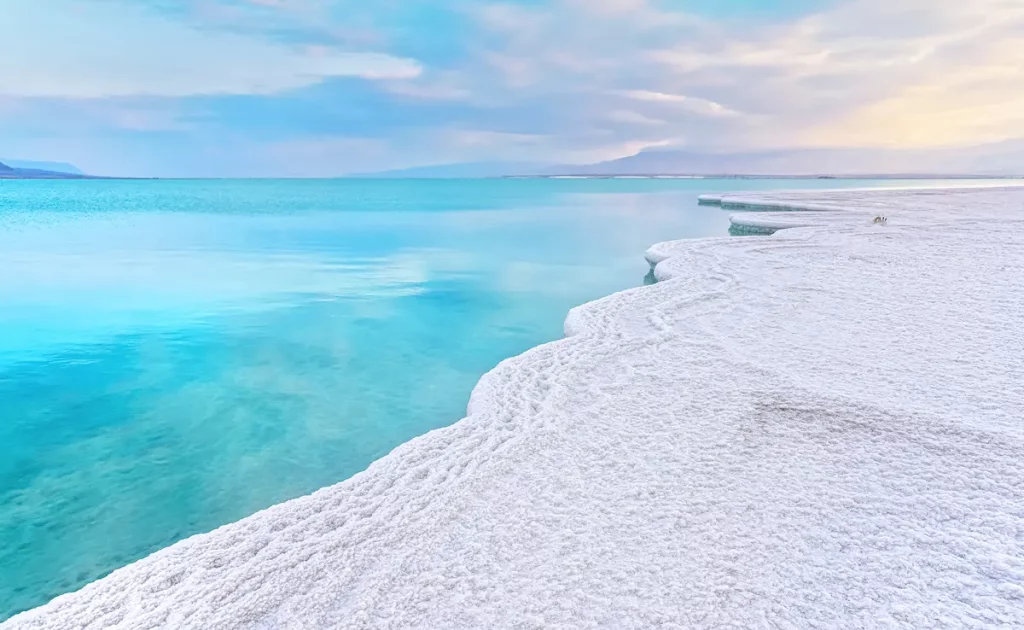 Morning scenery - white salt crystals beach, clear water near, typical landscape at Dead Sea shore