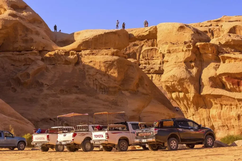 Bedouin jeep tour cars standing near Um Frouth stone bridge, desert with cliff rocky mountain in the background